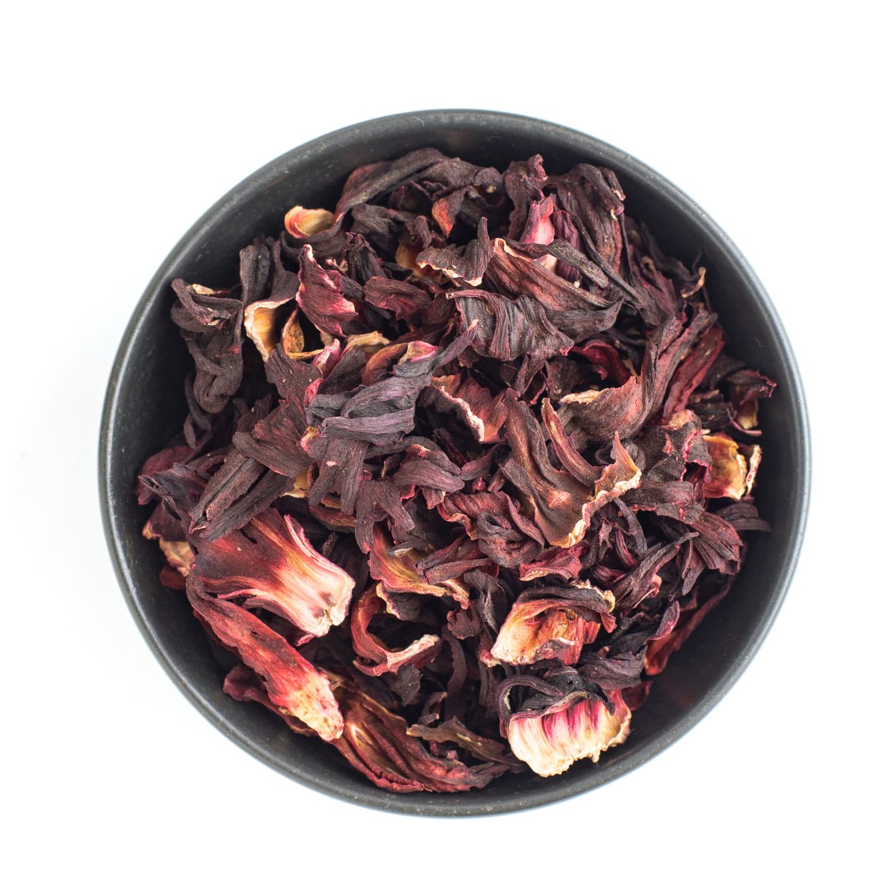 Dried hibiscus petals in dark bowl isolated on white background. Red tea, karkade. Top view.